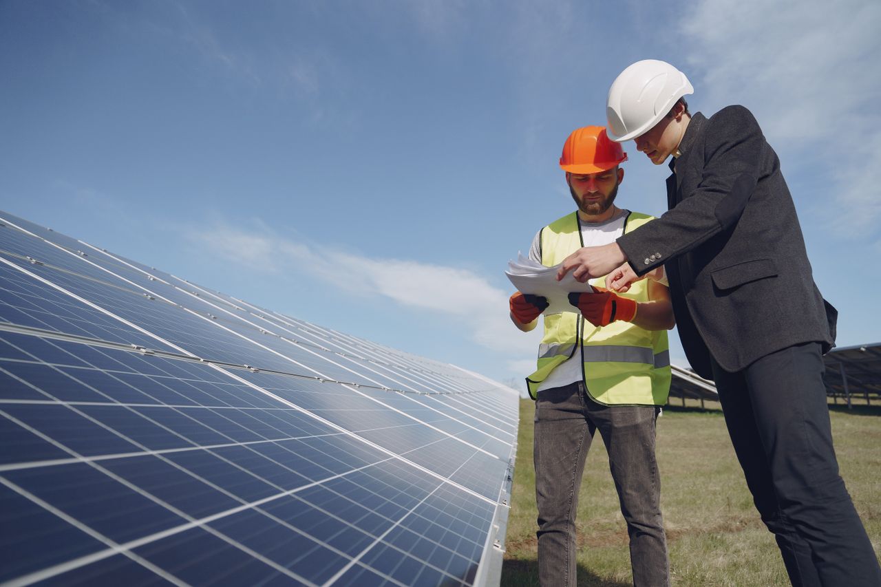 brand-03 Low angle of young inspector and foreman in hardhats checking documentation against modern solar panels in field