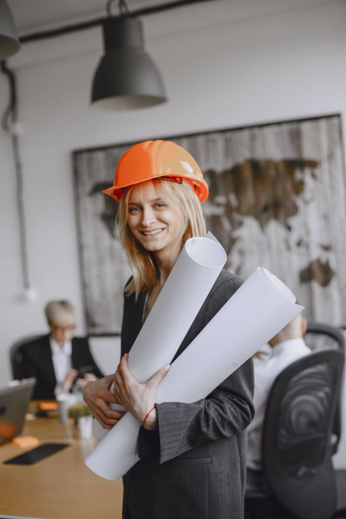 Mastering the First Impression: Your intriguing post title goes here Smiling female architect in hard hat holding blueprints in modern office setting.