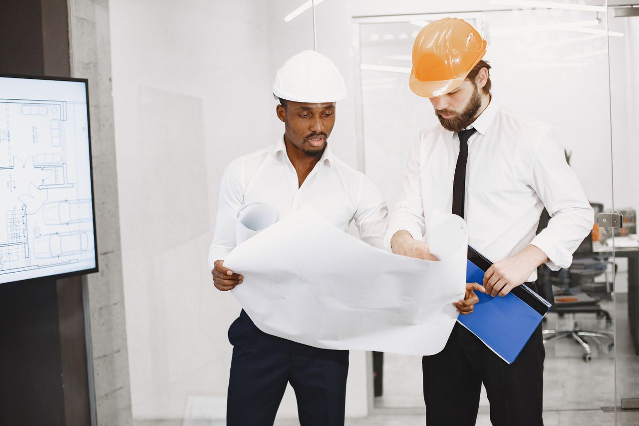 digital-01 Two architects in hard hats review blueprints during a collaborative meeting in an office setting.